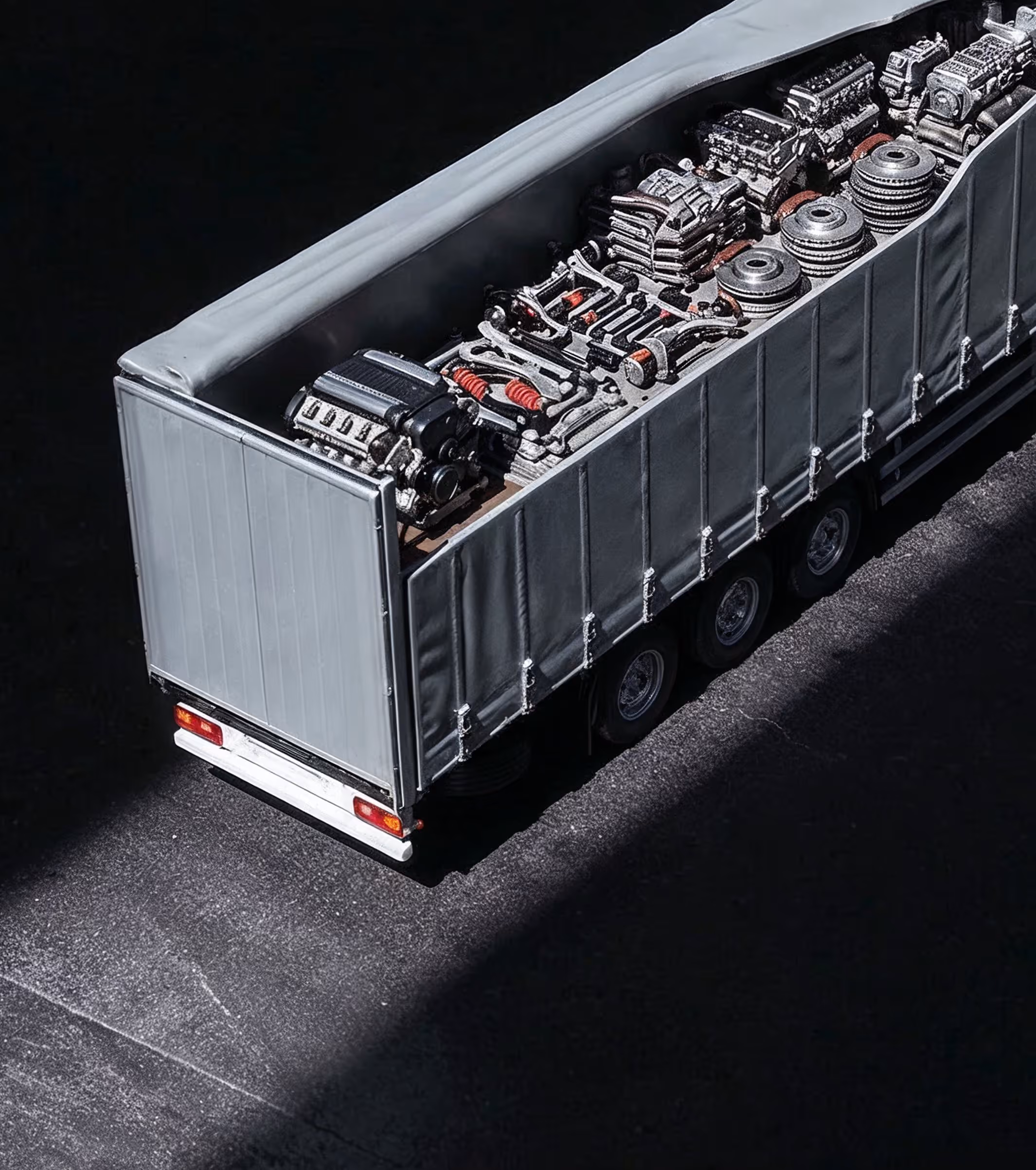 Truck with open gray tarp carrying various engine parts and mechanical components.